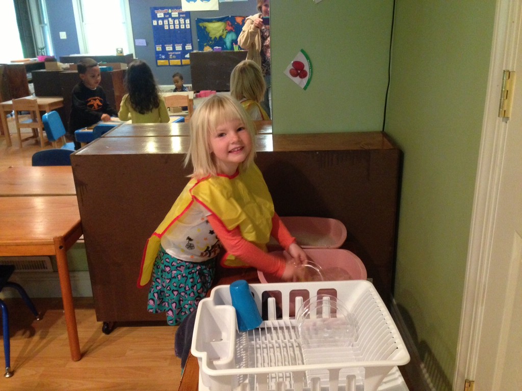 A 4-year old child is having fun washing her own dishes after having snack.